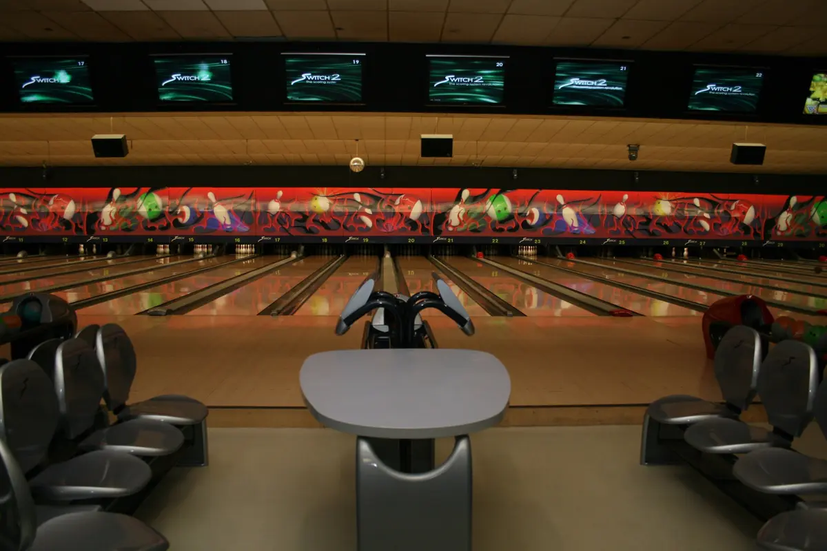 Bowlingcenter bei Nacht: Bahnen, Kugelrücklauf und Monitore über den Bahnen